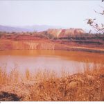 Mining dump in the background, red polluted water in the foreground